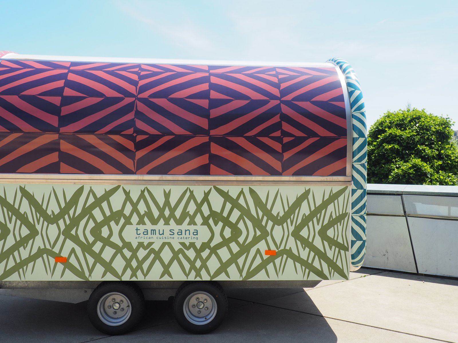 Der tamu sana Foodtrailer mit afrikanischem Muster, Seitenansicht mit Logo
